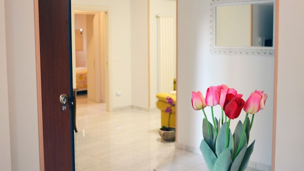 Un couloir avec une porte en bois, un miroir et un vase rempli de tulipes roses et rouges.