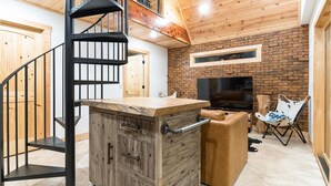 A modern interior with a wooden staircase, a kitchen island, a fireplace, and a TV.