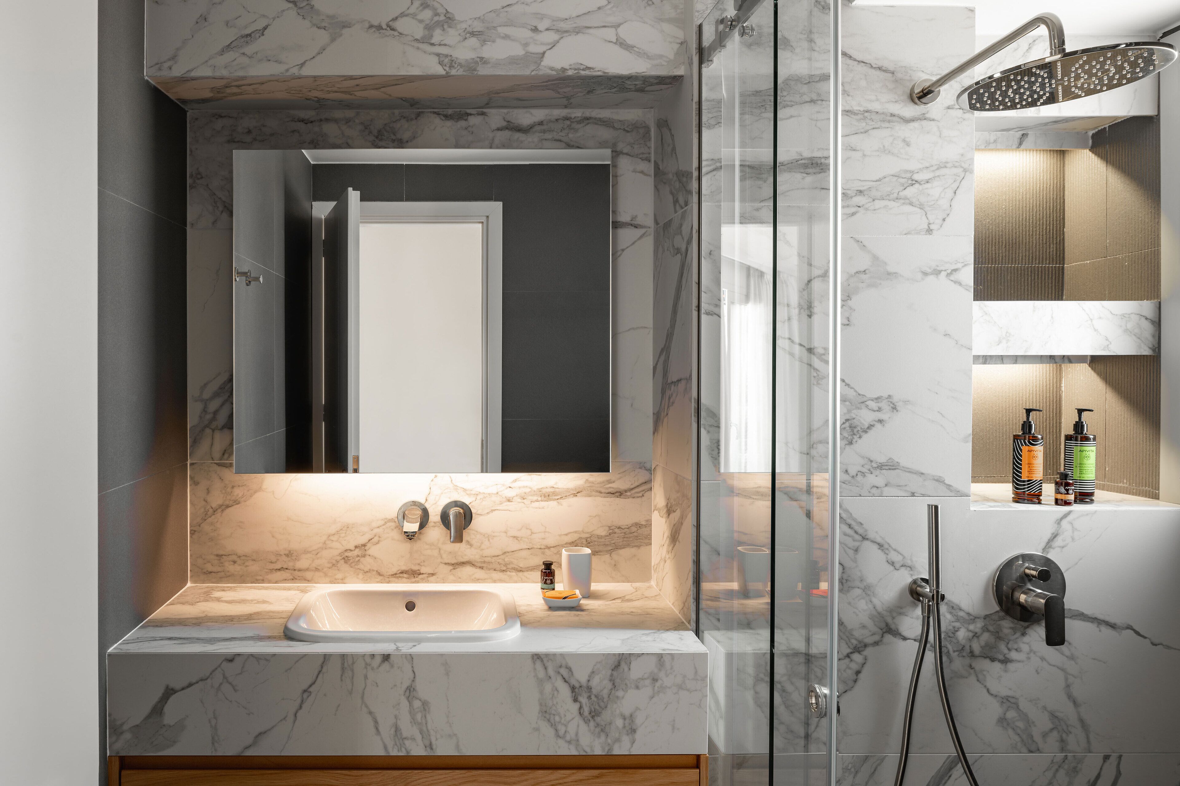 Une salle de bain moderne avec un lavabo en marbre, un miroir et une douche équipée d’un pommeau de douche à main.