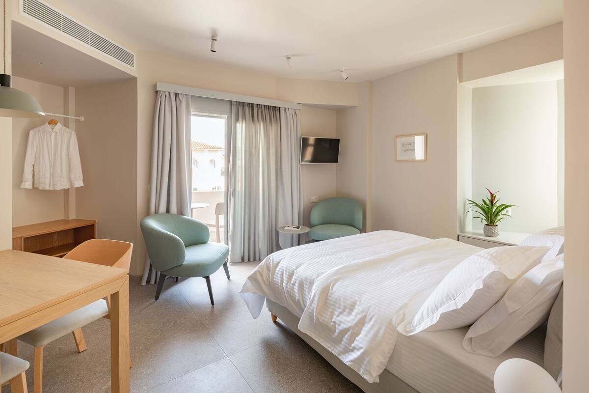 Habitación de hotel con cama, escritorio, silla, televisor y ventana con cortinas.