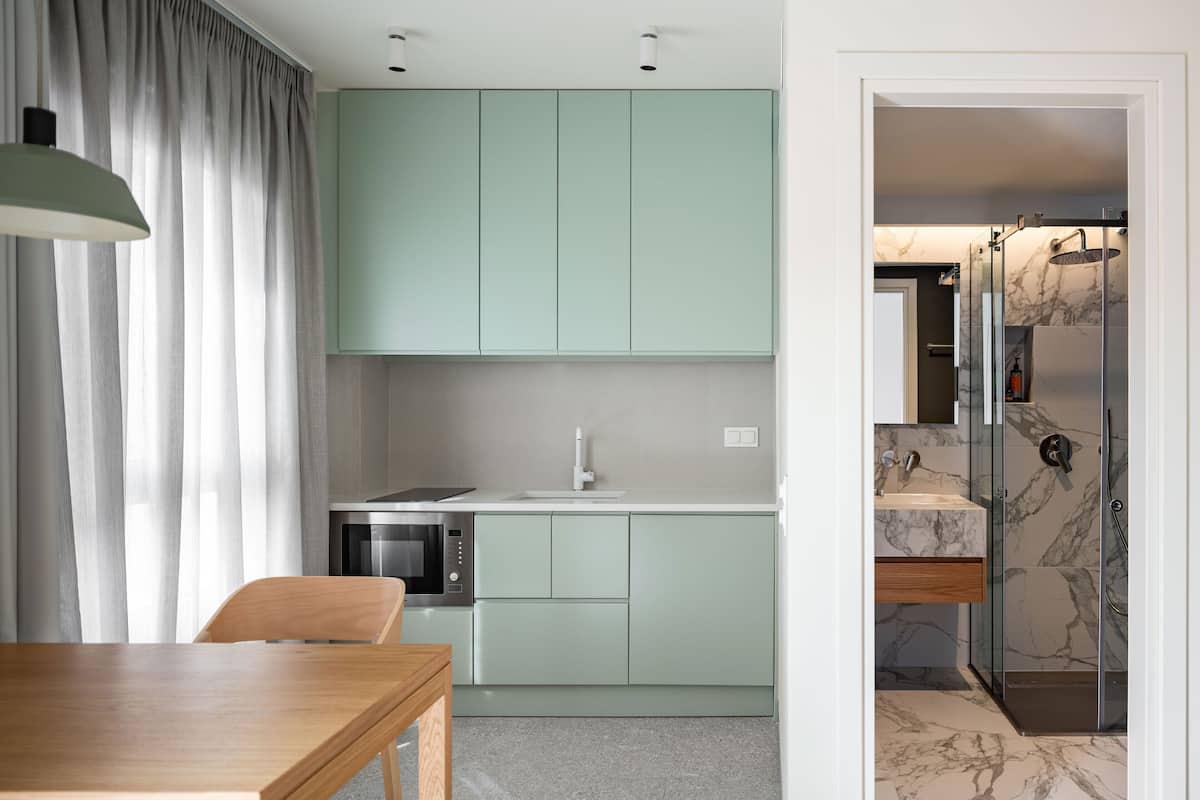 Una cocina moderna con armarios verde claro, una mesa de comedor de madera y un microondas integrado.