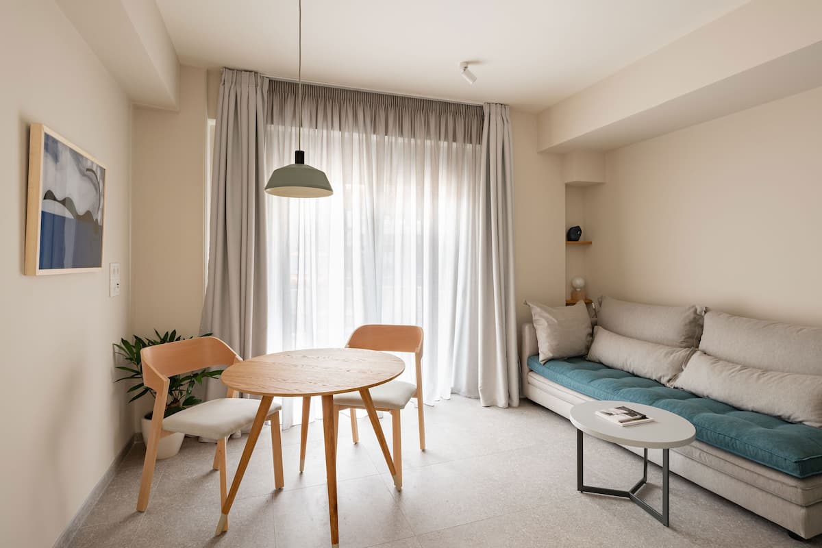 Un salón moderno con una mesa redonda de madera, dos sillas, un sofá con cojines color turquesa y una lámpara colgante.