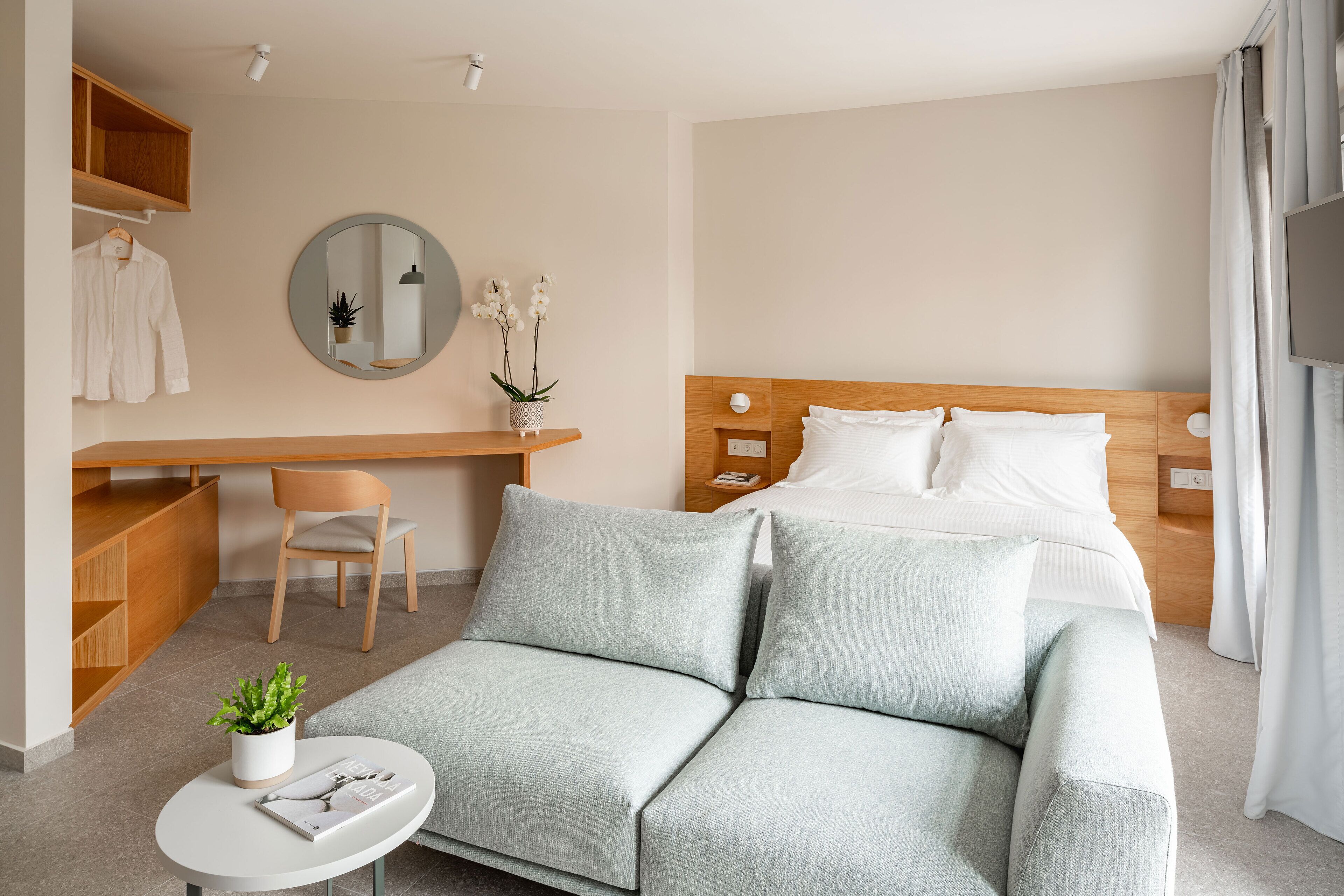 A modern hotel room with a bed, a sofa, a desk, and a chair.