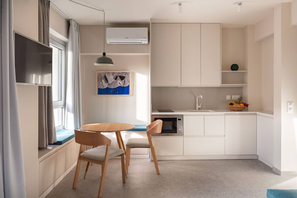 Una cocina moderna con comedor, muebles blancos, horno empotrado y ventana con cortinas.