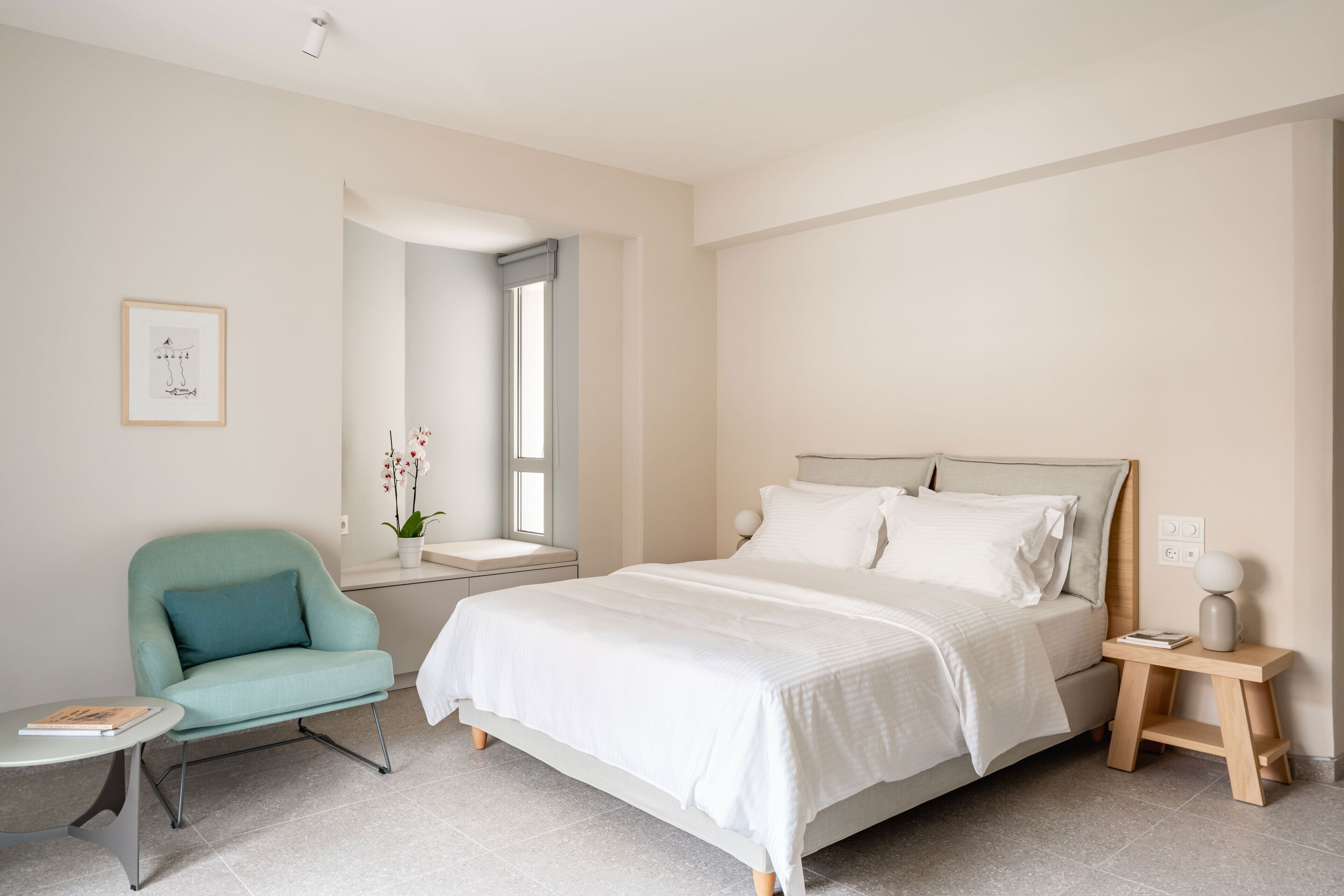 A modern bedroom with a bed, a chair, a bedside table, a nightstand, and a window.