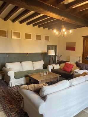 Uma sala de estar acolhedora com teto de madeira, um sofá verde, um sofá marrom e um tapete estampado.