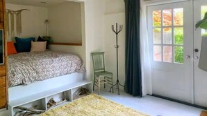 Une chambre à coucher comprenant un lit, une chaise, un porte-manteau et une porte donnant sur l’extérieur.