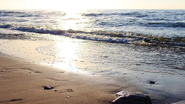 Ein Strand mit Wellen, Fußabdrücken und einem Felsen.