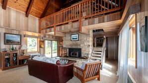 Un vaste salon doté d’une cheminée en pierre, d’un haut plafond en bois et d’une grande fenêtre.