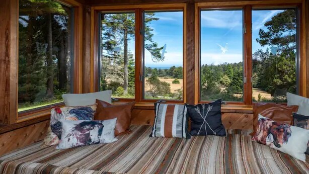 L’intérieur chaleureux d’un chalet avec un banc en bois, de grandes fenêtres et une vue sur une forêt.