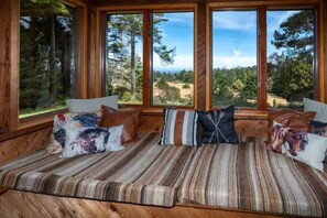 A cozy cabin interior with a wooden bench, large windows, and a view of a forest. - Hidden Gem! Great views, fireplace, stars & nature (Fort Bragg)