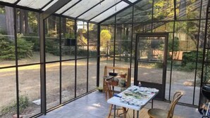 Une véranda avec une table et des chaises, de grandes fenêtres et une vue sur l’extérieur.