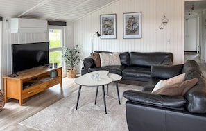 A living room with a TV, leather sofa, coffee table, and a potted plant.