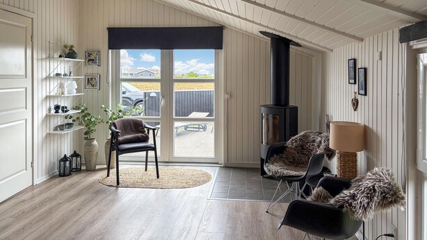 A room with a fireplace, wooden flooring, a seating area with chairs, a bookshelf, and a view through a glass door. - Awesome home in Ringkøbing with sauna (Ringkøbing)