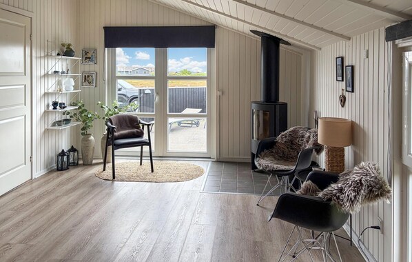 A room with a fireplace, wooden flooring, a seating area with chairs, a bookshelf, and a view through a glass door.
