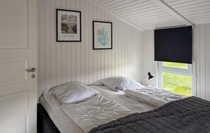 Une chambre à coucher avec un lit, deux tableaux encadrés, une fenêtre avec un store noir et une porte à serrure.