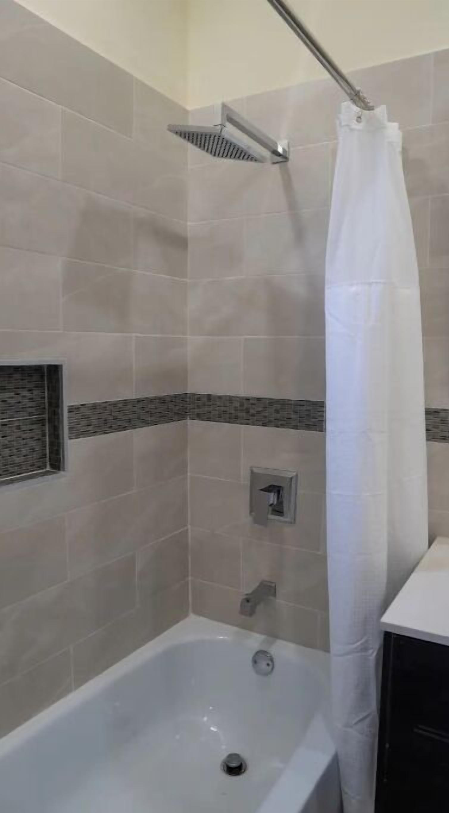 Een badkamer met een bad, een douche met gordijn en betegelde wanden.