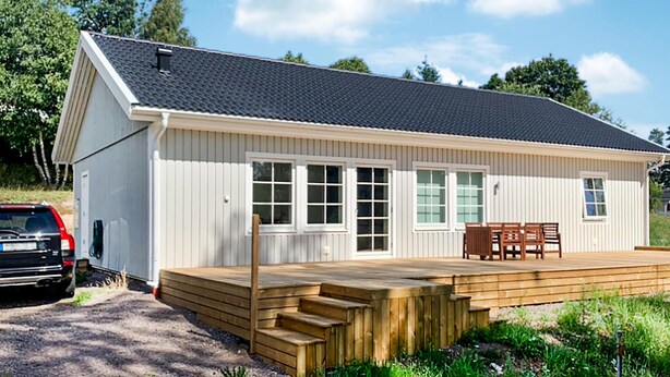 En etagers bygning med skråtag, en træterrasse og en bil foran.