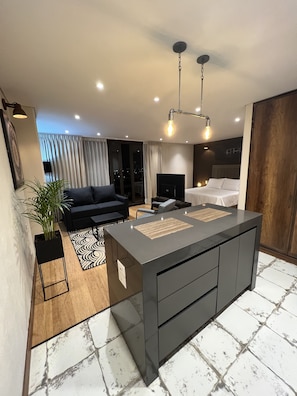 Een moderne hotelkamer met een centraal eiland, een bank, een televisie en een bed.