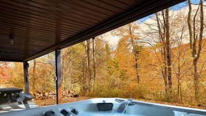 Un bain à remous sous un toit en bois, avec vue sur les arbres aux couleurs automnales.