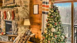 L’intérieur chaleureux d’un chalet avec une cheminée en pierre, un sapin de Noël et une vue par la fenêtre.