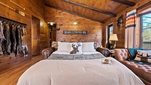 Une pièce chaleureuse aménagée dans un chalet en rondins, avec un grand lit, un canapé en cuir et un porte-manteau mural orné de peaux de fourrure.