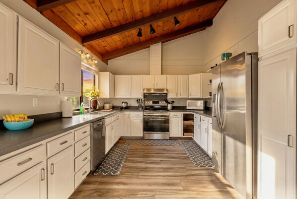 A kitchen with white cabinets, stainless steel appliances, and a wooden ceiling.
