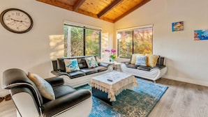 A modern living room with a wooden ceiling, two sofas, a coffee table, and large windows with a view of trees. - Coastal Retreat - 3,000 sqft, Pets Ok, Walk 2 Beach & Tidepools, Surf, see Seals (Moss Beach)