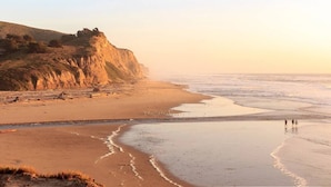 A beach with a rocky cliff and a few people walking along the shore. - Coastal Retreat - 3,000 sqft, Pets Ok, Walk 2 Beach & Tidepools, Surf, see Seals (Moss Beach)