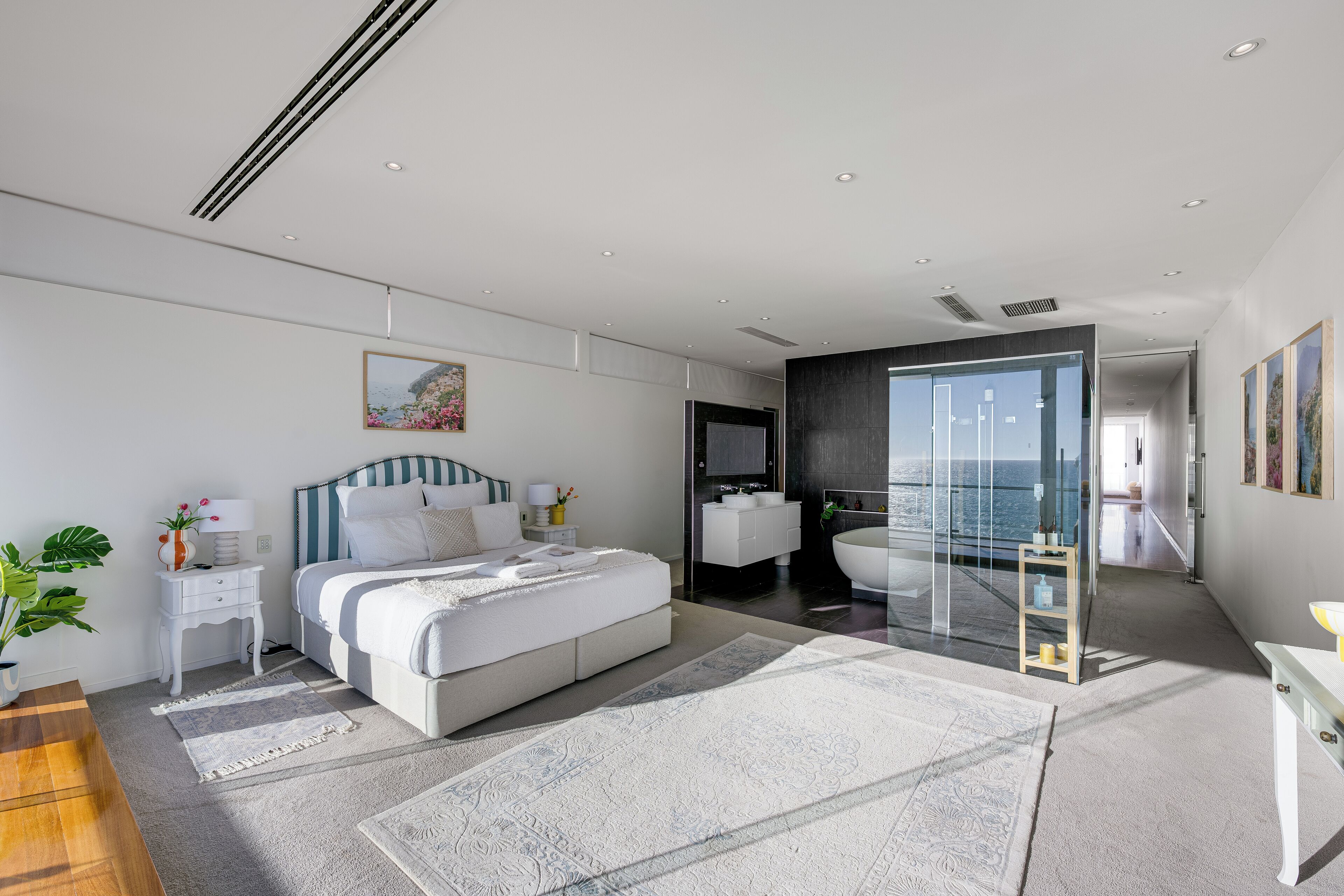 Une chambre à coucher moderne avec un grand lit, une table de chevet avec une lampe, une commode et une plante en pot.