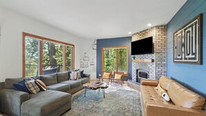 A modern living room with a fireplace, large windows, and a flat-screen TV mounted on the wall.