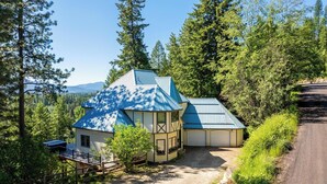 A cabin with a blue roof, surrounded by dense forest and mountains in the background.
