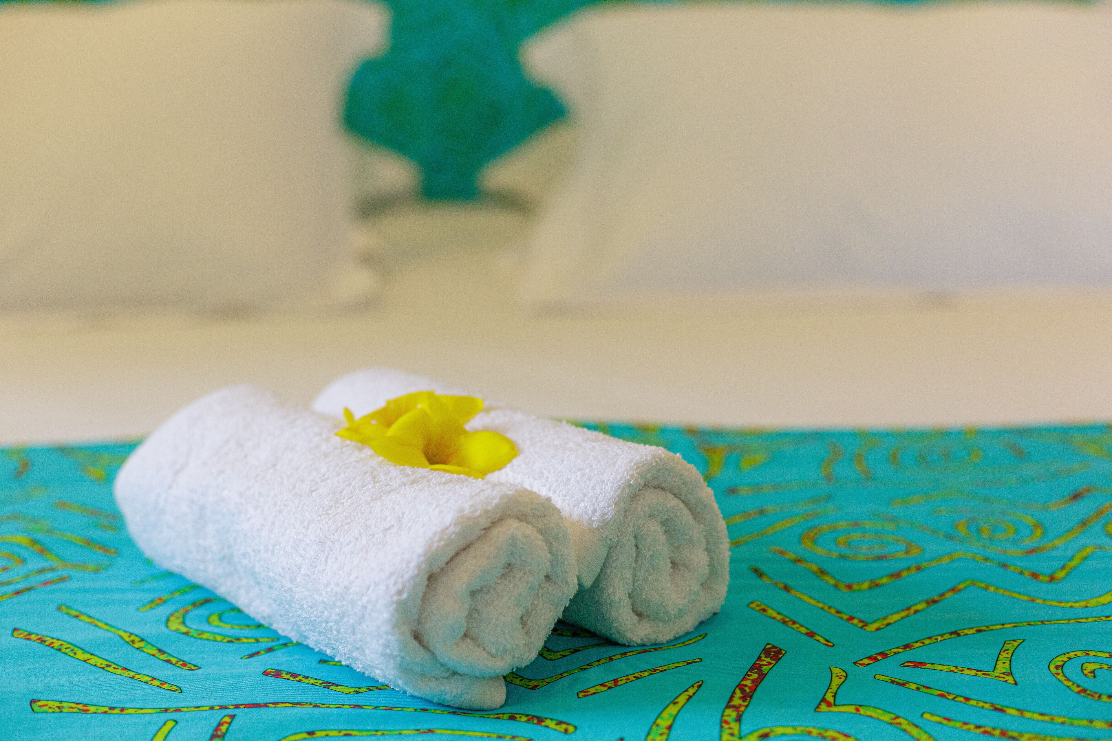A rolled white towel with a yellow flower on a blue patterned bedspread.