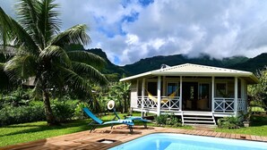 A poolside area with a wooden deck, lounge chairs, and a small building with a balcony. - FARE VAVAE (Raiatea)