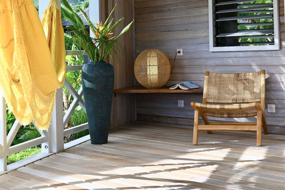 A covered porch with a wooden ceiling, a large potted plant, a wicker chair, and a yellow hammock.
