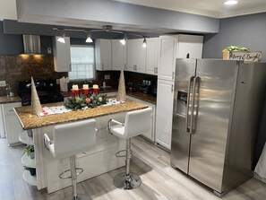 Eine moderne Küche mit weißen Schränken, einem Edelstahlkühlschrank und einer Arbeitsplatte aus Granit.
