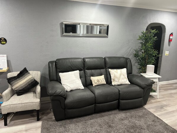 A modern living room with a black leather sofa, a grey armchair, and a grey carpet. - Create Family Memories (South Gate)