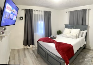 Ein Schlafzimmer mit Bett, Vorhängen, einem Fernseher und einer kleinen Pflanze.