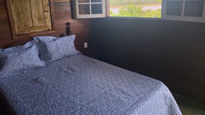 A room with a bed, a wooden wardrobe, and a window with a view of a landscape.