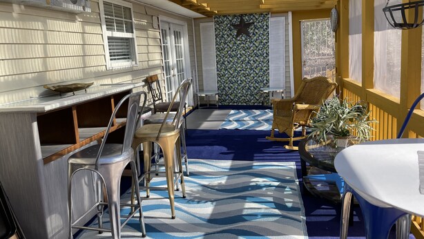 A sunlit patio with a blue and white patterned rug, metal chairs, a wicker rocking chair, and a white table. - Delightful, 4BR 2.5BA ranch style near Parks, trails, shops, malls, Restaurants. (Lithonia)