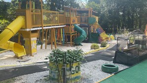 A playground with slides and climbing structures, surrounded by trees and a sandy area. - Delightful, 4BR 2.5BA ranch style near Parks, trails, shops, malls, Restaurants. (Lithonia)