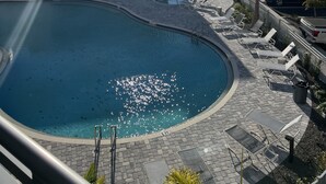 A swimming pool with a sunlit sky, lounge chairs, and a modern building in the background. - Apartment in Sarasota (Sarasota)