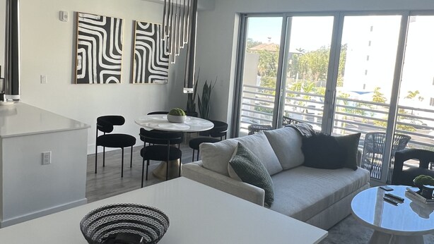 A modern living space with a dining area, a sofa, and large windows offering a view of the outdoors. - Apartment in Sarasota (Sarasota)