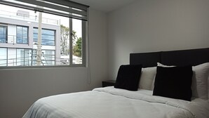 A bedroom with a bed, a nightstand, and a window with blinds. - Privated room with bathroom (Bogotá)