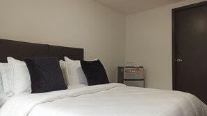 A hotel room with a bed, white bedding, dark headboard, and a refrigerator with magnets. - Privated room with bathroom (Bogotá)