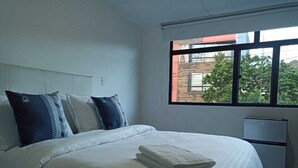 A hotel room with a bed, a window with a view of buildings, and a small refrigerator. - Privated room with bathroom (Bogotá)