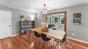 A dining area with a wooden table, black chairs, a chandelier, a bookshelf, and a painting on the wall. - Beaver Lake Getaway-15 min from downtown Rogers with HOT TUB! (Rogers)
