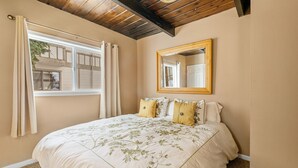 Ein Schlafzimmer mit einem großen Bett, einem Fenster mit Vorhängen, einer Holzbalkendecke und einem Spiegel an der Wand.