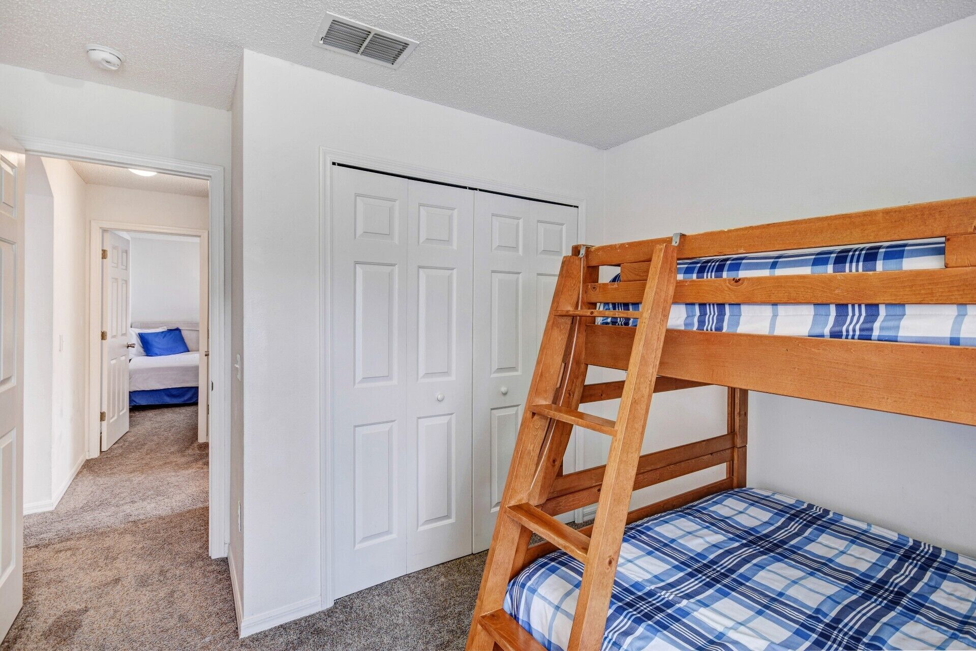 Uma cama de beliche com colchão xadrez em um quarto com paredes brancas e piso coberto de carpete.