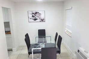 Un coin repas avec une table à plateau en verre, des chaises noires, un tableau abstrait en noir et blanc accroché au mur, et une fenêtre avec des stores.